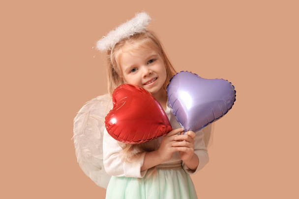 Χαριτωμένο κοριτσάκι ντυμένο ως Έρως με μπαλόνια σε σχήμα καρδιάς σε καφέ φόντο. Γιορτή του Αγίου Βαλεντίνου - Φωτογραφία, εικόνα