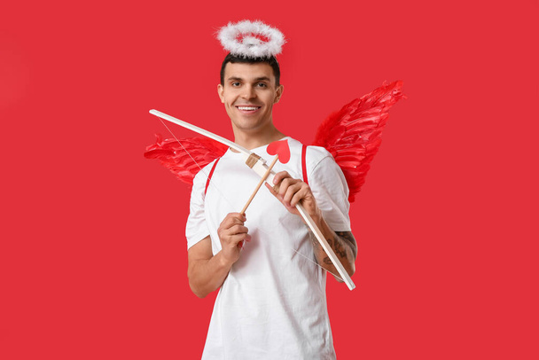 Jovem vestido de Cupido com arco no fundo vermelho. Celebração do Dia dos Namorados - Foto, Imagem