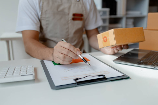 owner of an online store packs products into parcel boxes based on orders from online sales sites, packs products for delivery to addresses via private courier service. Product packaging concept. - Photo, Image