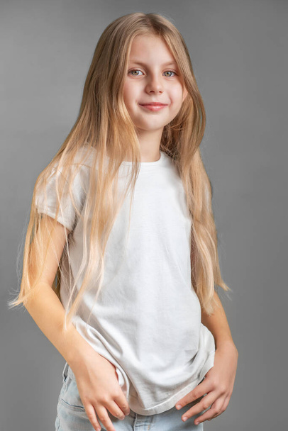 Портрет милой маленькой девочки с длинными светлыми волосами в белой футболке - Фото, изображение