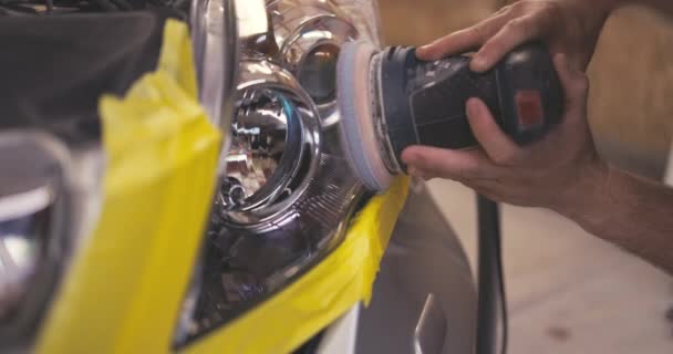 Καθαριστής αυτοκινήτων υπηρεσιών στίλβωσης αυτοκίνητο ειδικό προβολέα στίλβωσης με τη μηχανή γυαλίσματος στο γκαράζ εργαστηρίων - Πλάνα, βίντεο