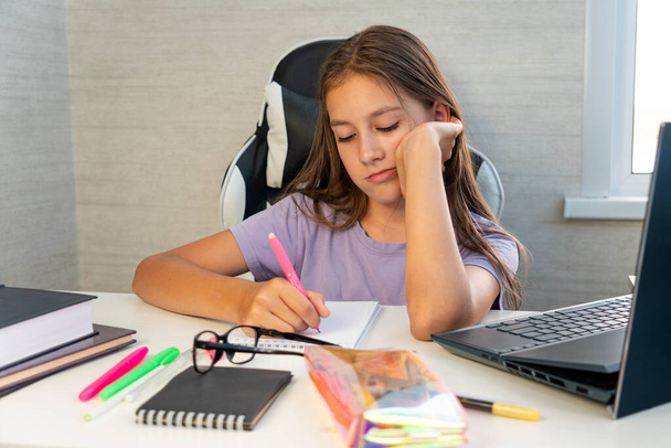 Gyermeknevelés. Unatkozó diák fáradt tanulás csinál házi feladat segítségével pc, szomorú tinédzser lány tanul felkészülés vizsga teszt, írás a copybook csinál irodalom kutatás - Fotó, kép