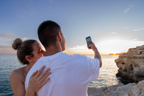 Een jong stel zonsondergang selfie op het strand: een close, horizontaal schot van achteren - Foto, afbeelding