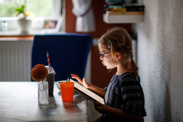 Tablet bilgisayarı elinde tutan pozitif küçük bir kız. Gözlüklü anaokulu çocuğu oyun oynuyor ve farklı uygulamalarla öğreniyor. - Fotoğraf, Görsel