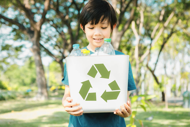 Iloinen nuori aasialainen poika tilalla kierrättää symboli bin päivänvalossa luonnon vihreä puisto edistää jätteiden kierrätystä, vähentää, ja käyttää uudelleen rohkaisua ekologisen kestävän tietoisuuden tuleville sukupolville. Kierrä - Valokuva, kuva