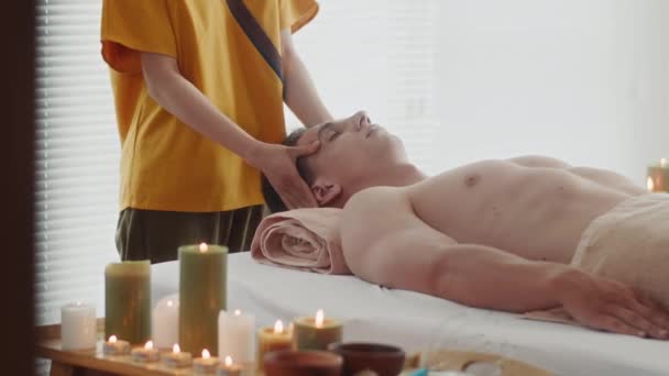 Обрізаний знімок жінки в жовтій формі дає масаж обличчя чоловічому клієнту під час сеансу терапії в салоні - Кадри, відео