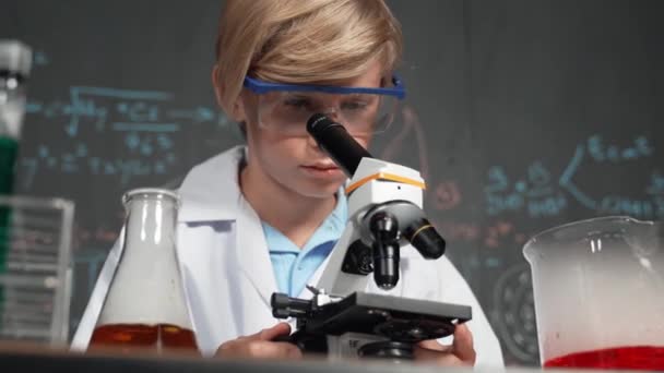 STEMサイエンスクラスまたは化学レッスンの科学実験室で顕微鏡分析サンプルを使用したスマート少年. チューブ内の化学液を検査するスコープの下を探している幸せな白人学生. エラー. - 映像、動画