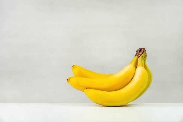 Słodkie banany na białym drewnianym stole na białym tle. przestrzeń kopiowania - Zdjęcie, obraz
