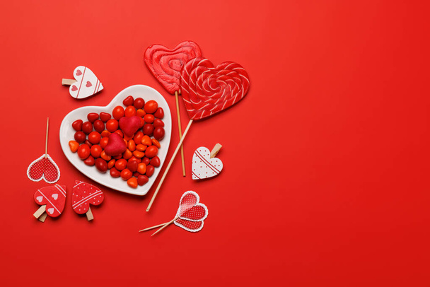 Piruletas del corazón: Dulces golosinas sobre un telón de fondo rojo con espacio de texto. Flat lay tarjeta de San Valentín - Foto, imagen