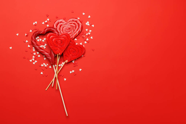 Lizaki serca: Słodkie przekąski na czerwonym tle z przestrzenią tekstową. Flat lay Walentynki karty - Zdjęcie, obraz