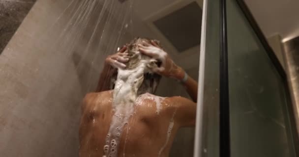 Vrouw wast haar lange haar met shampoo onder de douche. Vrouwen haarverzorging - Video