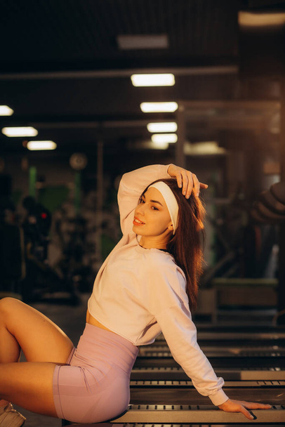Bonito retrato comercial de fitness fitness atleta femenina sonriente casual en el gimnasio cerca de la máquina de correr. Foto de alta calidad - Foto, Imagen