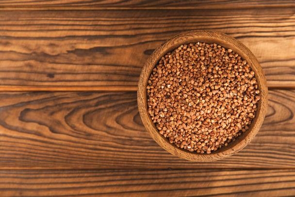 Raw buckwheat in a bowl on a textured wooden background. Wheat grains, porridge, cereals, raw buckwheat in a plate. Healthy food. Porridge. Diet. Organic cerea. Space for text.Copy space. - Photo, Image
