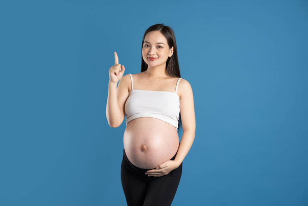 Porträt einer schwangeren Asiatin, isoliert auf blauem Hintergrund - Foto, Bild