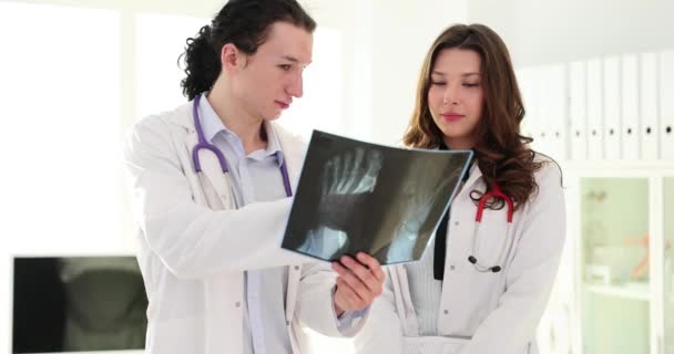 Врачи мужчина и женщина смотрят на рентген ступни в клинике. Медицина и радиология - Кадры, видео