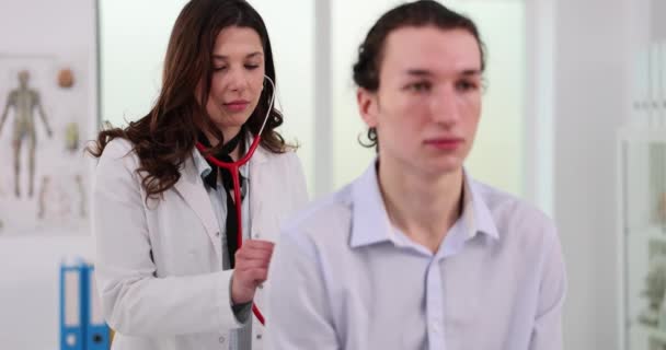 Терапевт слухає дихання підлітка зі стетоскопом. Уважний лікар-жінка вивчає пацієнта з кашлем у клініці - Кадри, відео