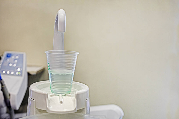 wegwerpbeker met vloeistof voor het spoelen van tanden in een tandartspraktijk op een lichte achtergrond. Tandheelkundige verzorging en behandeling - Foto, afbeelding