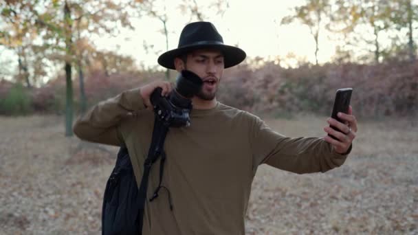 Mannelijke reiziger die selfie portret poseert in het herfstbos met camera in zijn hand. Natuurfotograaf maakt zelffoto op mobiele telefoon. Kopieerruimte - Video