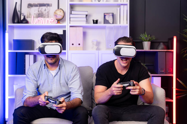Buddy ystävä pelaajat pelaavat videopeliä joysticks ja VR kuulokkeet virtuaalisen teknologian todellisuudessa studiohuoneessa neon sininen valo. Mukava elää sisätiloissa iloinen taistelevat voittaja. Myytävissä. - Valokuva, kuva