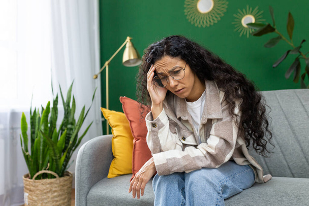 Mulher solitária deprimida sentada no sofá na sala de estar em casa, mulher hispânica infeliz pensando enquanto se inclina nos braços. - Foto, Imagem