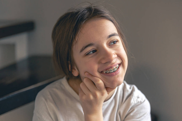 Μια έφηβη με σιδεράκια χαμογελάει στο σπίτι, δείχνοντας τα δόντια της. Ορθοδοντική έννοια της θεραπείας. - Φωτογραφία, εικόνα