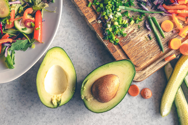 Verse groenten gesneden op een snijplank op de keukentafel, bovenaanzicht. Avocado en andere groenten tijdens het koken van de salade. - Foto, afbeelding