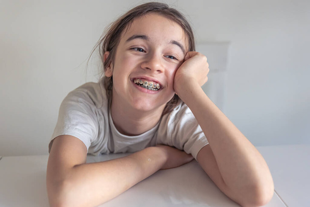 Забавная девочка-подросток смотрит в камеру и демонстрирует брекеты на зубах. Концепция ортодонтического лечения и стоматологического здоровья. - Фото, изображение