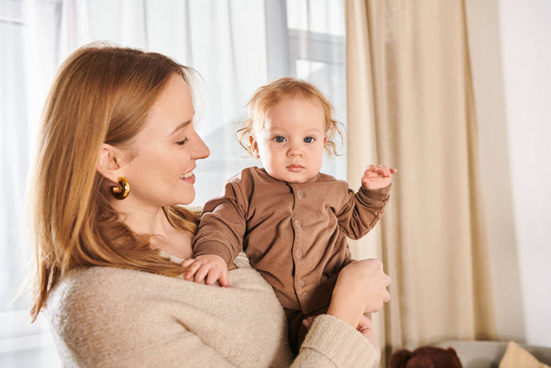 radostná žena drží malého chlapečka v rukou v dětském pokoji doma, blažené mateřství - Fotografie, Obrázek
