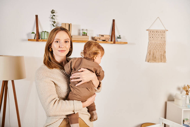szczęśliwa młoda kobieta trzyma i przytula małego synka w pokoju dziecinnym, błogie macierzyństwo - Zdjęcie, obraz