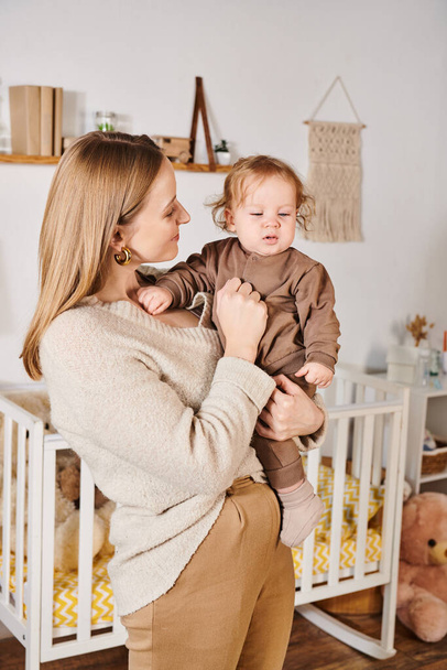 jeune femme attrayante tenant adorable petit fils dans une chambre d'enfant confortable, maternité heureuse - Photo, image
