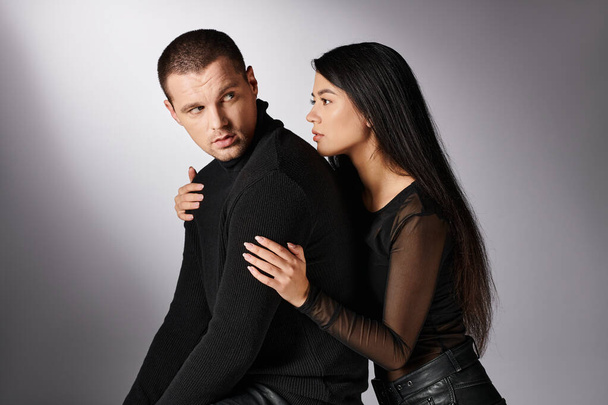 young attractive asian woman hugging offended man sitting on grey backdrop, fashion and relationship - Foto, Bild