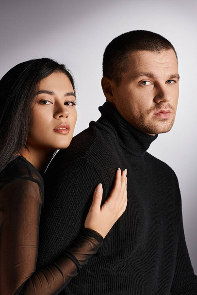 expressive interracial couple in black outfit looking at camera on grey backdrop with lighting - Photo, Image
