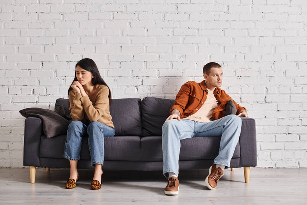 Oturma odasında kanepede otururken gözlerini kaçıran depresif ırklar arası çift, boşanma kavramı. - Fotoğraf, Görsel