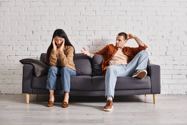 リビングルームのソファーで怒ったアジアの女性と話す若い男,関係の困難 - 写真・画像
