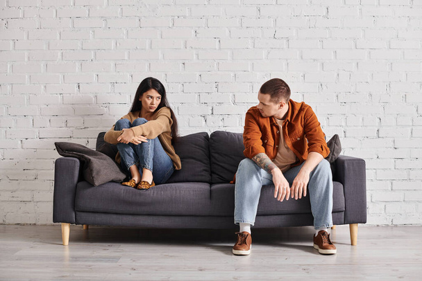 frustrovaný mezirasový pár dívá na sebe na gauči v obývacím pokoji, rozvod koncept - Fotografie, Obrázek
