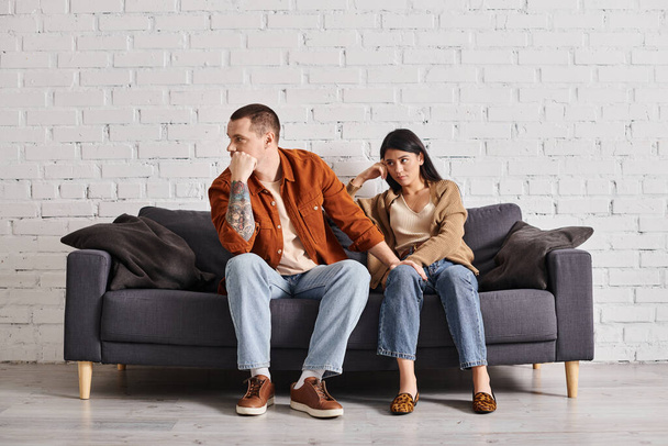 νεαρό διαφυλετικό ζευγάρι σε φιλονικία κάθεται στον καναπέ στο σαλόνι στο σπίτι, έννοια του διαζυγίου - Φωτογραφία, εικόνα