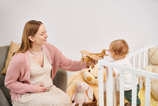 mulher grávida alegre brincando com avião de brinquedo e pequeno filho n quarto de crianças em casa, maternidade feliz - Foto, Imagem