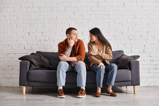 family divorce, offended asian woman talking to smiling skeptical husband on couch in living room - Photo, Image