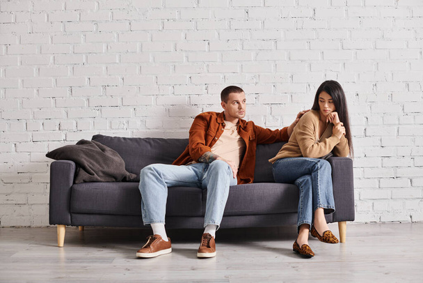 fiatal férfi nyugtató ideges ázsiai feleség ül kanapén a nappaliban, kapcsolat nehézségek - Fotó, kép