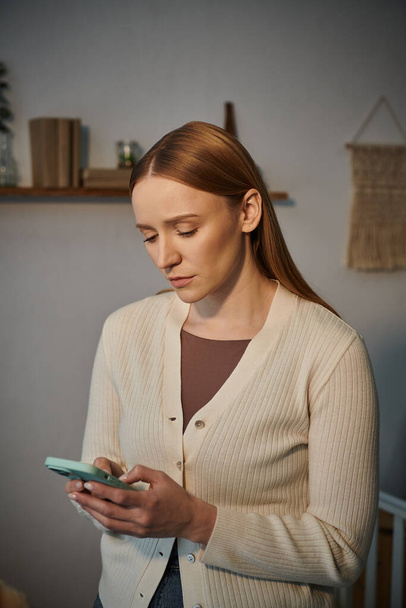 frustrado e chateado jovem mulher mensagens no telefone celular em quarto escuro berçário em casa - Foto, Imagem