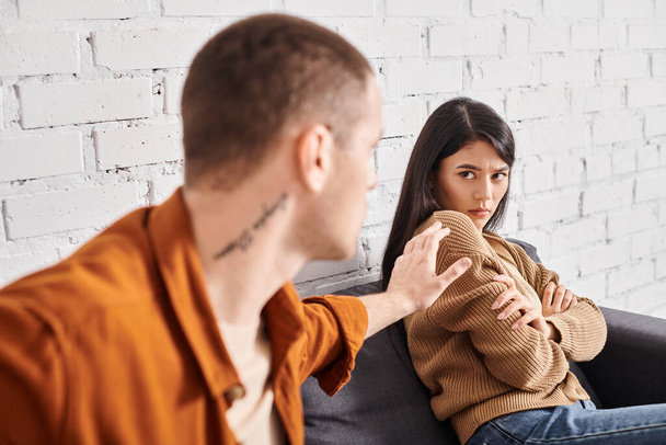 молодий чоловік намагається заспокоїти азіатську дружину, сидячи на дивані вдома, проблеми з відносинами - Фото, зображення