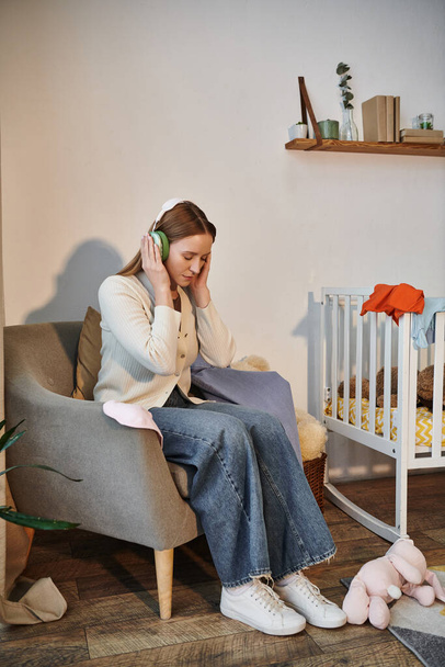 gefrustreerde vrouw probeert te ontspannen door te luisteren naar muziek in koptelefoon in donkere kinderkamer thuis - Foto, afbeelding