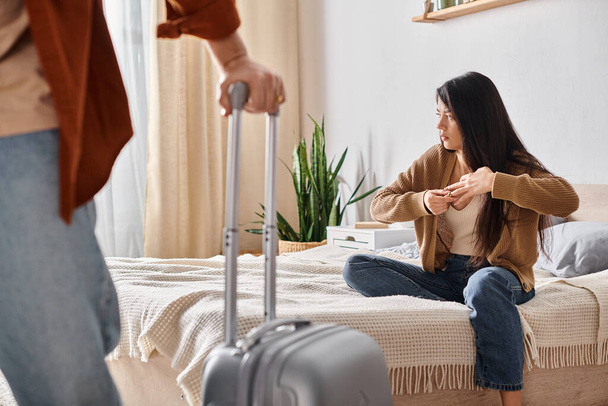 beleidigte Asiatin zieht Ehering aus, während ihr Mann mit Koffer das Haus verlässt, Scheidung - Foto, Bild