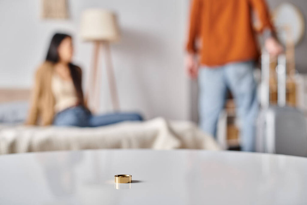 селективный фокус обручального кольца на столе возле межрасовой пары, ссорящейся в спальне, развод - Фото, изображение