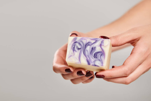 объект фото полосатой полоски мыла в руках неизвестной женщины с лаком для ногтей на сером фоне - Фото, изображение