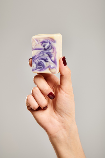 objeto foto de la barra de jabón rayado púrpura en la mano de una mujer desconocida posando sobre fondo gris - Foto, imagen