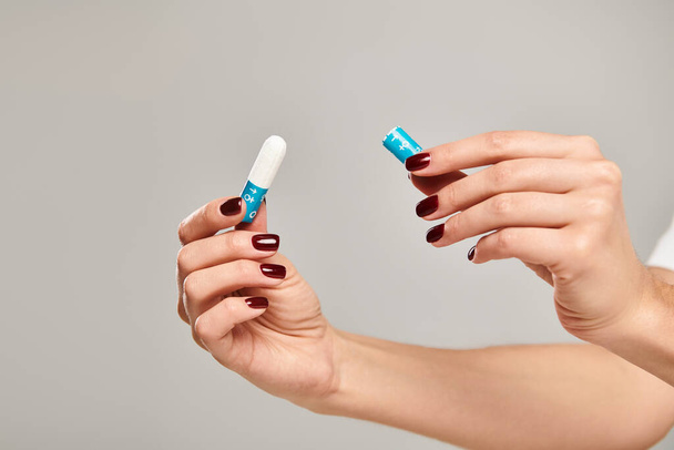 hygienic tampon in hands of unknown young female with nail polish on gray backdrop, object photo - Photo, Image