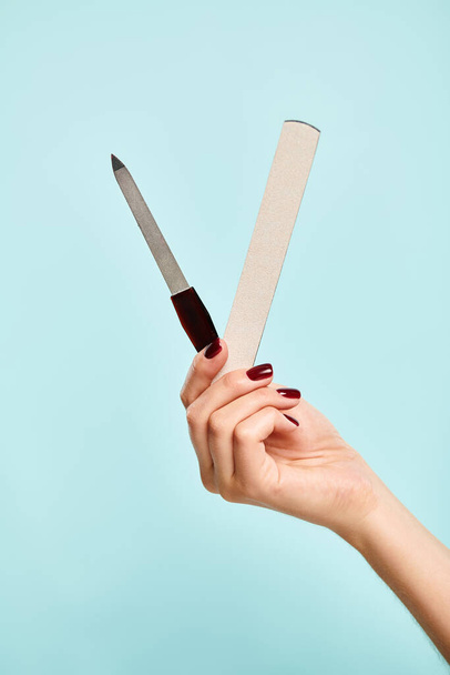 two nail files in hand of unknown young  woman with nail polish on blue backdrop, object photo - Photo, Image