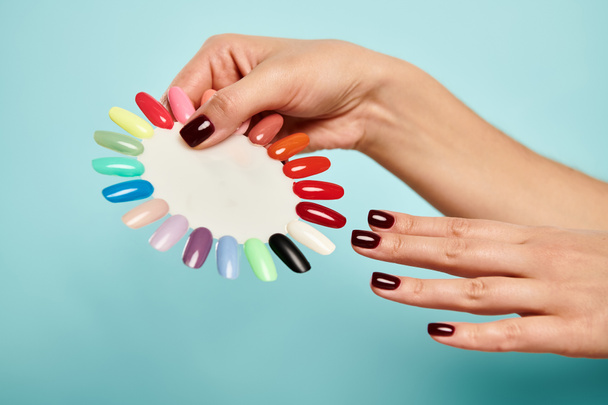 young unknown woman holding nail polish palette in hands on vibrant blue background, object photo - Photo, Image