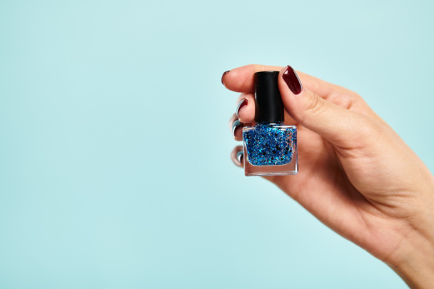 об'єкт фото синього яскравого лаку для нігтів в руці молодої невідомої жінки синього фону - Фото, зображення